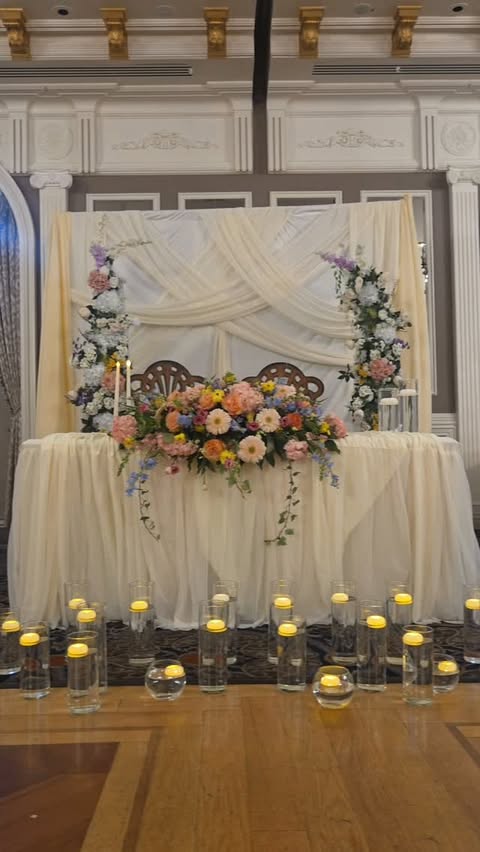 Candlelit sweetheart table with drapery and florals at a wedding reception